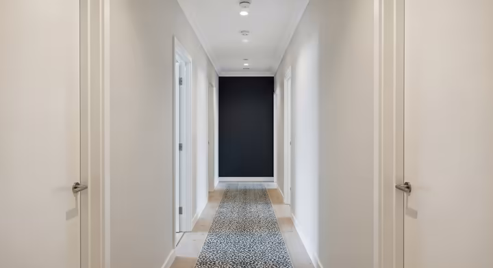 A long, narrow hallway where the end wall is painted a dark charcoal gray, creating an optical illusion that makes the hallway appear wider and shorter.