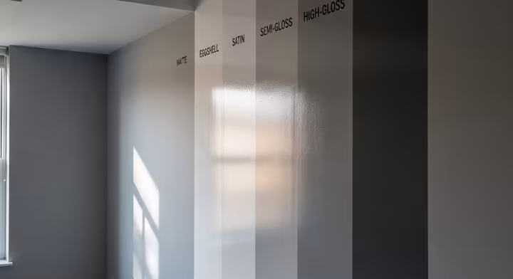 A wall painted with vertical stripes of different paint sheens, from matte on the left to high-gloss on the right, showing how each reflects light differently.