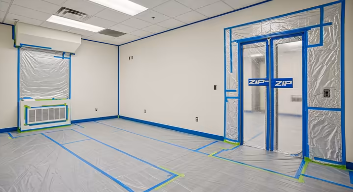 A well-sealed renovation work area showing a plastic zip-wall system for entry, sealed HVAC vents, and plastic-covered floors.